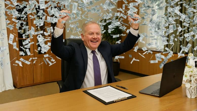 Man in a business suit sitting at a desk, smiling and raising his arms as money rains down around him, representing Brian Kelly celebrating his $20 million buyout.
