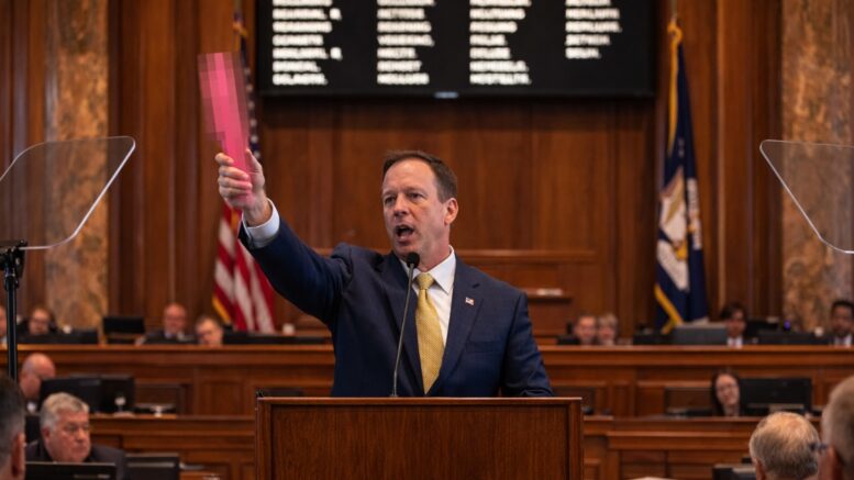 Louisiana lawmaker speaking at the senate podium holding a censored pink object during debate over a proposed Sx activity tax.