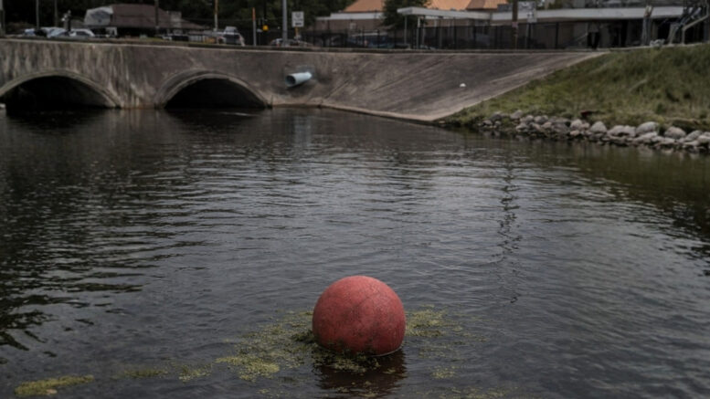 Red playground ball floating in canal water in Metairie near New Orleans, urban drainage canal with algae, local Louisiana news image.