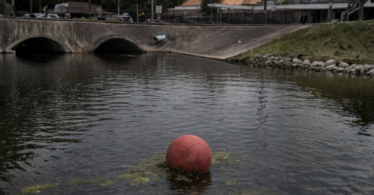 Red playground ball floating in canal water in Metairie near New Orleans, urban drainage canal with algae, local Louisiana news image.