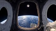 View from inside Artemis II spacecraft window showing Earth’s curved horizon and the Moon in space, with a small “Just Say N.O.” sticker placed beside the window frame inside the capsule.