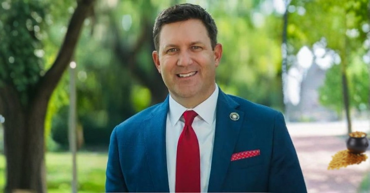 Jefferson Parish Councilman Scott Walker smiling in a suit with a small pot of gold in the background.