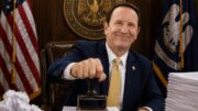 Gov. Jeff Landry stamps a stack of official papers in a government office, symbolizing a suspended recall petition.