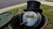 An illustration of a wealthy, sentient smart water meter wearing a top hat, monocle, bow tie, and cigar while sitting inside an open underground utility box beside a residential street.